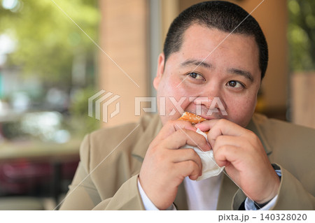 Plus size Isan Thai businessman eating a hamburger at a restaurant Plus size Isan Thai businessman eating a hamburger at a restaurant 140328020