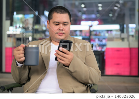 Plus size Isan Thai businessman using phone and holding a mug outdoors Plus size Isan Thai businessman using phone and holding a mug outdoors 140328026
