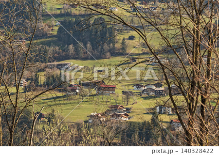 Looking trough tree branches on a village in a valley Looking trough tree branches on a village in a valley 140328422