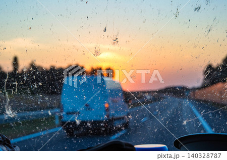 Sunset view through a dirty car windshield on the highway with a van in motion, focusing on travel, visibility, and road safety concerns. Transportation, logistics, road traffic. Copy space 140328787