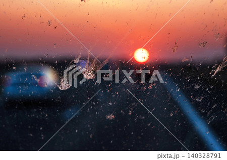 Blurry highway through a smudged dirty car windshield, affecting visibility during orange sunset, emphasizing traffic safety concerns and the importance of clean glass for safe travel. Blurry highway through a smudged dirty car windshield, affecting visibility during orange sunset, emphasizing traffic safety concerns and the importance of clean glass for safe travel. 140328791