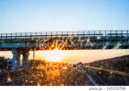 Highway and bridge at sunset through a dirty windshield, emphasizing road safety and the challenges of visibility while driving on long journeys. Transportation, logistics, road traffic. Copy space 140328796
