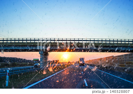 Highway and bridge at sunset through a dirty windshield, emphasizing road safety and the challenges of visibility while driving on long journeys. Transportation, logistics, road traffic. Copy space Highway and bridge at sunset through a dirty windshield, emphasizing road safety and the challenges of visibility while driving on long journeys. Transportation, logistics, road traffic. Copy space 140328807