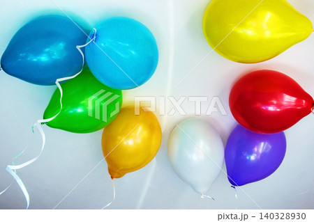 Group of multicolored vibrant helium balloons with ribbons in red, blue, yellow, green, purple, and white hanging from a ceiling, perfect for party themes or event decorations. Copy space 140328930