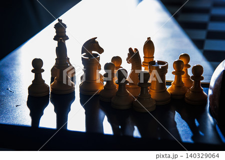 Chess pieces in sunlight on a blue tournament table after the endgame. Closeup of white chess pieces with a dramatic light effect, emphasizing intellectual depth of chess. Selective focus Chess pieces in sunlight on a blue tournament table after the endgame. Closeup of white chess pieces with a dramatic light effect, emphasizing intellectual depth of chess. Selective focus 140329064
