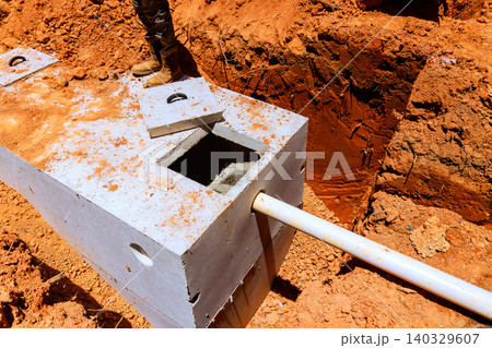 Workers install concrete septic tank into trench at construction site ground is dry with some dirt, rocks. 140329607