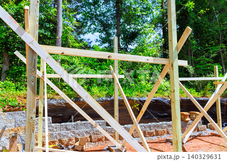 Workers set up wooden frames beams supports to shed at construction site surrounded by trees Workers set up wooden frames beams supports to shed at construction site surrounded by trees 140329631