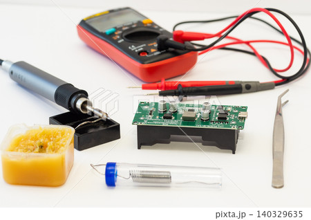 A multimeter with test probes, a soldering iron, and tools lie on a white background. 140329635