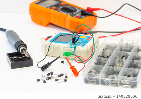 A multimeter with test probes, a soldering iron, and tools lie on a white background. 140329636