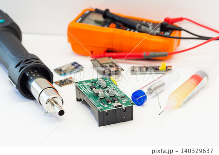 A multimeter with test probes, a hot air gun, and tools lie on a white background. 140329637