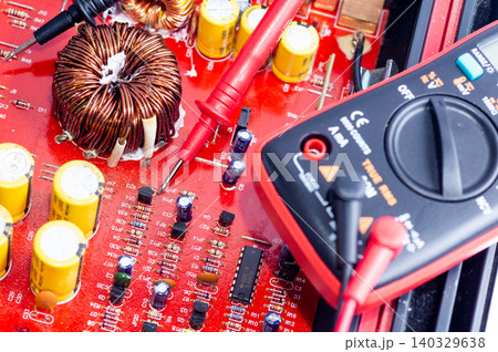 A multimeter with test probes and a circuit board lie on a white background. 140329638