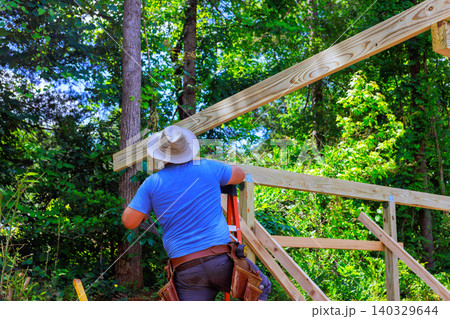 Worker climbs ladder to install beams for wooden project in construction works zone 140329644