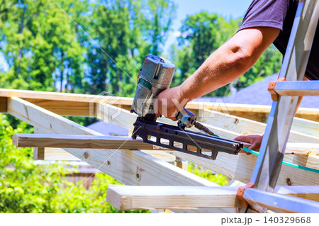 Worker climbs ladder to secure wooden beams with air nail gun. Worker climbs ladder to secure wooden beams with air nail gun. 140329668