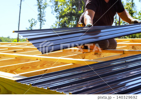Roofing worker places metal roofing sheets on wooden structure in construction area 140329692