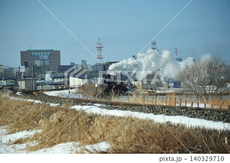 白煙を上げて走るSL冬の湿原号と釧路の街並み 140329710