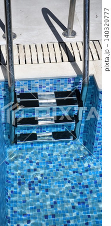 Swimming pool staircase with blue mosaic tiles and sun reflections 140329777