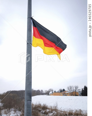 A German flag flutters in the wind against a winter landscape on a bridge. 140329785