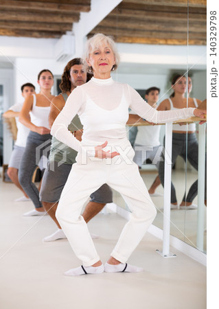 Senior woman and group of adult dancers practice ballet moves in classical dance school. Senior woman and group of adult dancers practice ballet moves in classical dance school. 140329798