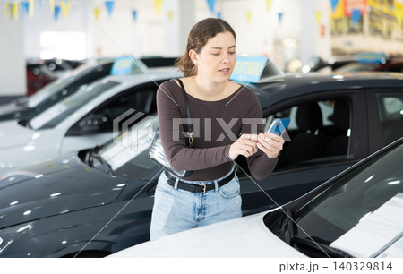 Young woman scanning QR code while choosing car at dealership 140329814