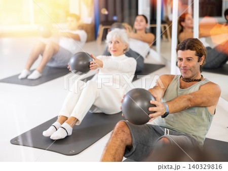 Middle-aged man practicing pilates with ball on gray mat in gym room Middle-aged man practicing pilates with ball on gray mat in gym room 140329816