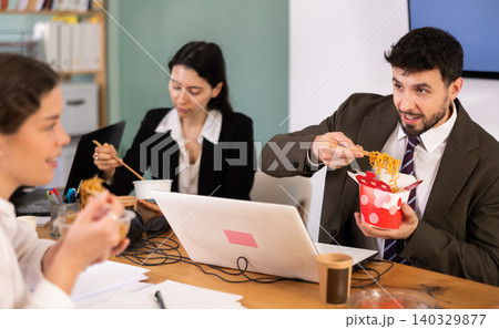 Group of colleagues, man and woman, are having lunch in office during their break, eating noodles Group of colleagues, man and woman, are having lunch in office during their break, eating noodles 140329877