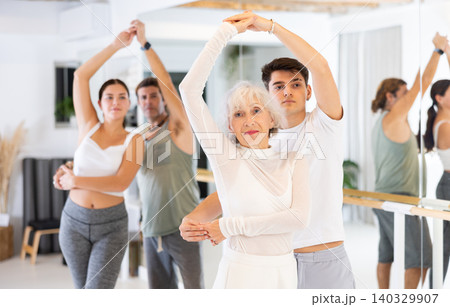 Elderly pretty woman and a young man are rehearsing a pair dance in a modern studio. Elderly pretty woman and a young man are rehearsing a pair dance in a modern studio. 140329907