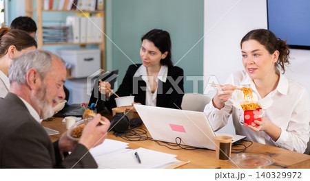 Group of colleagues, man and woman, are having lunch in office during their break, eating noodles Group of colleagues, man and woman, are having lunch in office during their break, eating noodles 140329972
