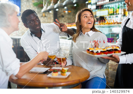 Positive Latin waiter in apron pointing hand on plate with pinchos in the middle of the bar Positive Latin waiter in apron pointing hand on plate with pinchos in the middle of the bar 140329974