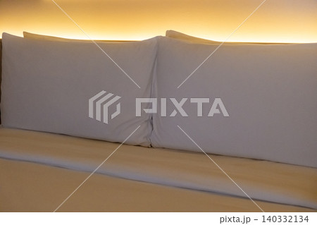 A neatly made hotel bed with soft pillows with uplight at the headboard A neatly made hotel bed with soft pillows with uplight at the headboard 140332134