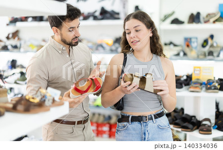 Young woman choosing sandals, her male partner helps at shoe store Young woman choosing sandals, her male partner helps at shoe store 140334036