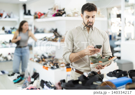 While shopping and choosing shoes, man scans QR code on toeless shoes While shopping and choosing shoes, man scans QR code on toeless shoes 140334217