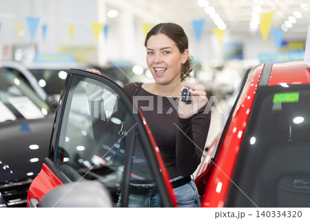 Young woman holding keys to new car in dealership Young woman holding keys to new car in dealership 140334320