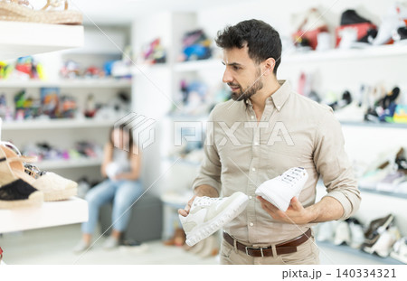 Man shopper in shoe store is looking at sneakers Man shopper in shoe store is looking at sneakers 140334321