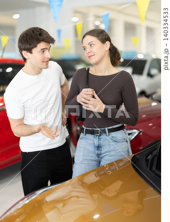Young in a car dealership chooses a car Young in a car dealership chooses a car 140334533