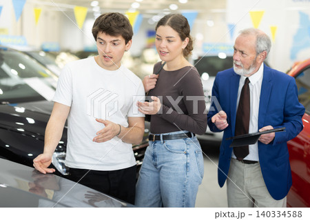 Senior salesman advises a young at a car dealership Senior salesman advises a young at a car dealership 140334588