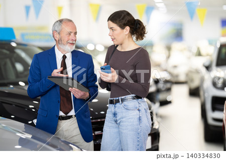 Elderly auto salesman advises a client, answering her questions 140334830