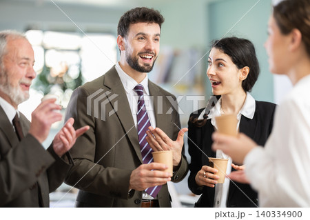 Group of positive office workers drink coffee and chat during work break in office of business company Group of positive office workers drink coffee and chat during work break in office of business company 140334900