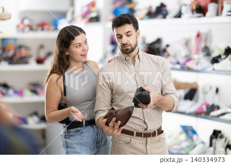 Man chooses classic shoes in shoe store. Young woman helps him with this 140334973