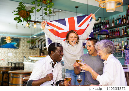 Happy sport fans holding flag of the Great Britain, celebrating victory of national team, drinking alcoholic drinks in pub Happy sport fans holding flag of the Great Britain, celebrating victory of national team, drinking alcoholic drinks in pub 140335271