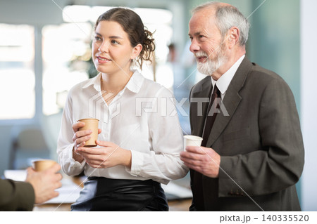 Young woman and man co-worker employees drinking coffee and talking during break while working in office Young woman and man co-worker employees drinking coffee and talking during break while working in office 140335520