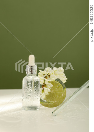 Serum bottle stands with a green slice and white flowers nearby Serum bottle stands with a green slice and white flowers nearby 140335529