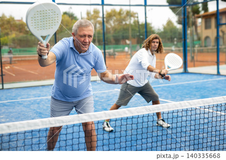 Focused mature man playing doubles paddle tennis Focused mature man playing doubles paddle tennis 140335668