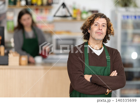 Working days in bakery, man worker of mini bakery prepares to meet cafe visitors. Working days in bakery, man worker of mini bakery prepares to meet cafe visitors. 140335699