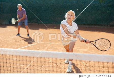 Elderly playing tennis together in court Elderly playing tennis together in court 140335733