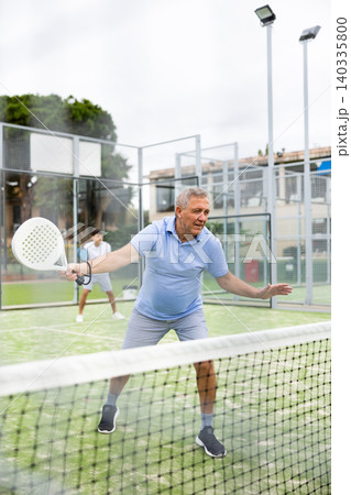 View through the tennis net at an elderly player in game of padel View through the tennis net at an elderly player in game of padel 140335800
