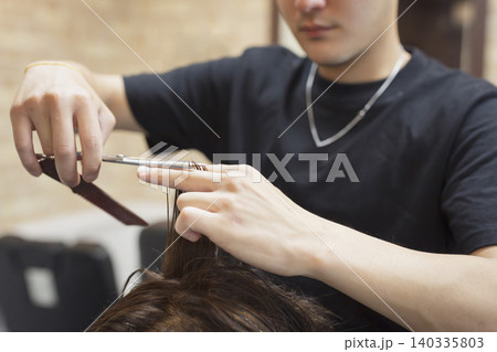 ヘアサロンで真剣な表情で男性客の髪をカットする男性美容師のクローズアップ 140335803