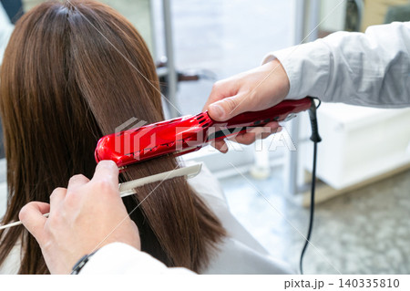 美容院でヘアアイロンを使って顧客の髪をストレートに伸ばすスタイリストの手元 美容院でヘアアイロンを使って顧客の髪をストレートに伸ばすスタイリストの手元 140335810