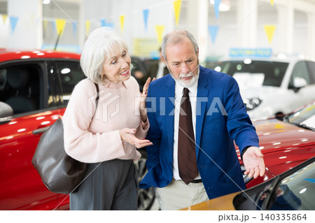 salesman shows a car to an elderly woman at a car dealership salesman shows a car to an elderly woman at a car dealership 140335864
