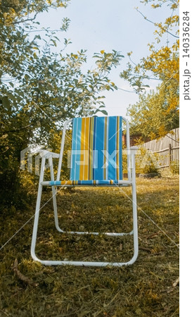 Blue and Yellow Striped Deck Chair in Garden with Trees and Grass Blue and Yellow Striped Deck Chair in Garden with Trees and Grass 140336284