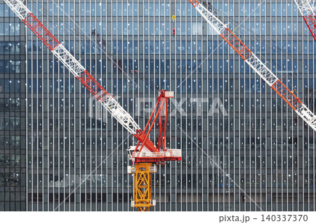 近代的なビルのガラスファサードを背景に立つ建設現場の大型タワークレーン 近代的なビルのガラスファサードを背景に立つ建設現場の大型タワークレーン 140337370